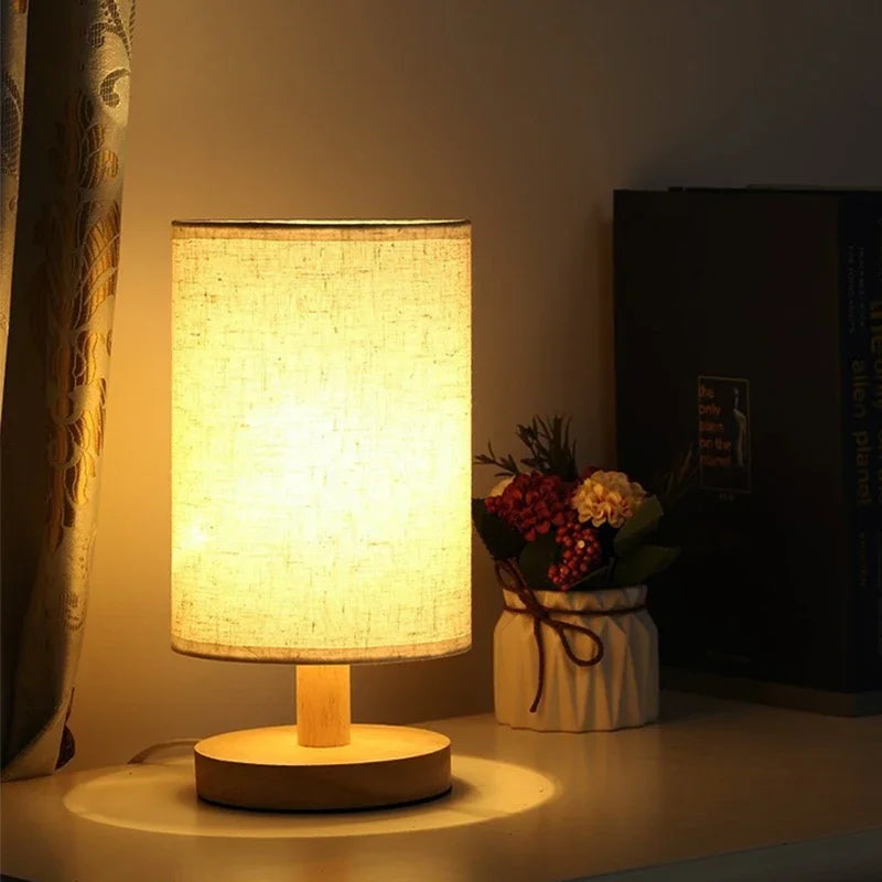 Table lamp with a soft glow on a surface next to a vase of flowers in a dimly lit room.
