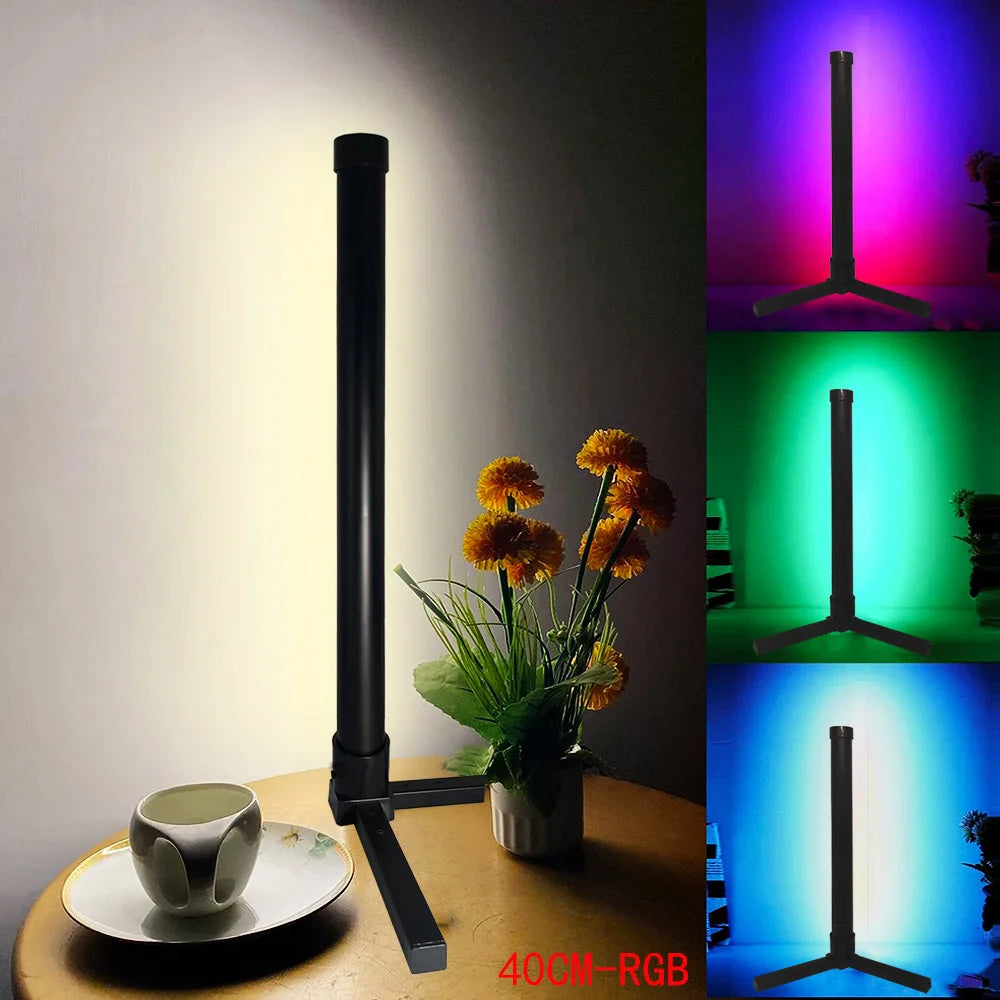Black LED light stand with RGB color changes on a table with flowers and a cup.